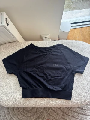 Svart croppad topp från ICANIWILL - Svart croppad topp från ICANIWILL med korta ärmar och bred resår nedtill. Toppen har en sportig look och är tillverkad i ett lätt och stretchigt material, perfekt för träning eller en avslappnad stil.