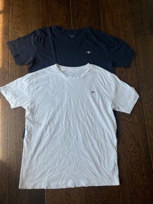 Gant t-shirts i vitt och marinblå - Säljer två stilrena t-shirts, en vit och en marinblå. Båda har rund hals och korta ärmar. Diskret liten logga på bröstet. Perfekta till jeans eller shorts för en enkel och clean look.