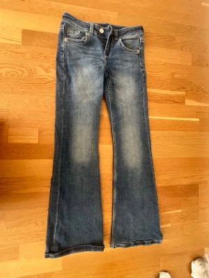 Blå bootcut jeans med slitningar - Säljer ett par blå bootcut jeans med snygga slitningar framtill och bakfickor med dekorativa sömmar och knappar. Jeansen har klassisk femficksmodell och är tillverkade i denim med lätt stretch. Från h&m Dem är för små i midjan men jag är 173 och dem passar perfect i längden.
