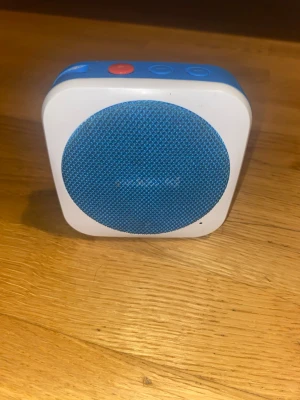 Polaroid blå portabel högtalare - Snygg portabel högtalare från Polaroid i vit och blå färg. Högtalaren har en rundad fyrkantig form, blått tyg över högtalaren och tydliga knappar på ovansidan. Perfekt för att ta med sig överallt tack vare sin kompakta design. Men logan är bort tagen, annars funkar den fint och de går utmärkt att ansluta till högtalaren. Och ljudet funkar utmärkt.