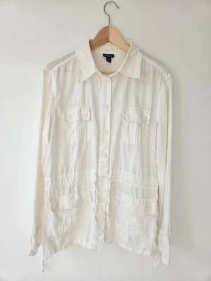 Vit linneskjorta jacka från Gant - Klassisk vit skjorta jacka från Gant i svalt linne. Skjortan har långa ärmar, fyra fickor framtill med knappar och en rak passform. Perfekt till sommaren och enkel att styla med det mesta. Stängs med knappar hela vägen framtill.