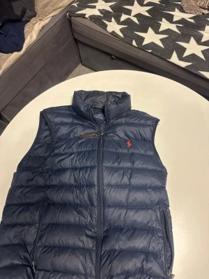 Mörkblå dunväst från Polo Ralph Lauren - Skön mörk blå väst från Ralph lauren, bra skick och sparsamt använd storlek medium, har ni några funderingar är det bara att kontakta mig