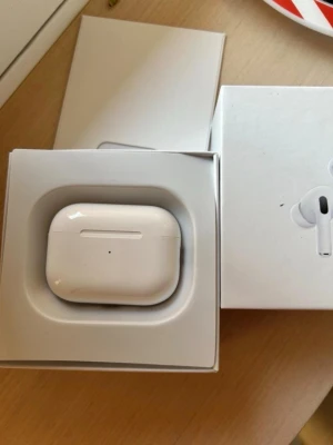 Airpods gen 2 - Säljer ett par vita trådlösa in-ear hörlurar med laddningsetui och laddningskabel. Snygg och kompakt design i blank plast, perfekt för dig som vill ha smidiga hörlurar till mobilen. Allt levereras i originalförpackning.
