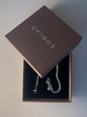 Silvrigt pärlarmband från Edblad - Snyggt armband från Edblad i silverfärg med små glittrande pärlor runt hela bandet. Justerbar längd med karbinlås och en liten Edblad-logga vid låset. Perfekt accessoar för att lyfta din outfit. Välj gärna instabox 