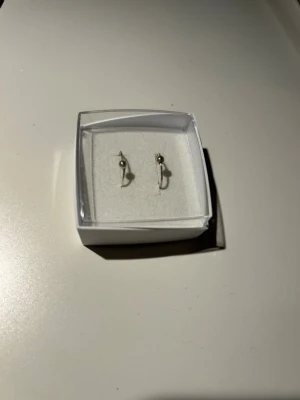 Silverfärgade örhängen med pärldetalj - Stilrena örhängen i silverfärgad metall. Örhängena är runda hoops med en liten pärldetalj på varje ring för att kunna öppna. Perfekta för dig som gillar minimalistisk och modern design. Oanvända
