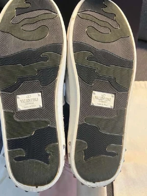 Blåa sneakers från Valentino - Snygga sneakers från Valentino i blå mocka med vita detaljer och vit sula. Skorna har en unik mönstrad yttersula och coola nitar runt hälen. Perfekta för dig som vill ha något extra till din outfit.