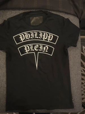Svart Philipp Plein t-shirt med tryck - Cool svart t-shirt från Philipp Plein med stort vitt tryck på bröstet. Klassisk rund halsringning och korta ärmar. Perfekt för dig som gillar streetwear och vill sticka ut med en tydlig logga. Original priset är 1200+