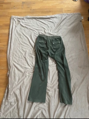 Mörkgröna mjukisbyxor med raka ben - Mörkgröna mjukisbyxor i mjukt velourmaterial med raka ben och fickor både fram och bak. Byxorna har resår i midjan och en avslappnad passform som är perfekt för chill dagar. Snygg detalj med ficklock bak och breda benslut.