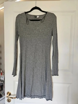 Klänning tunika H&M divided 40 - Grå klänning tunika från H&M divided 40  Säljer en grå ribbad klänning från H&M i storlek 40. Klänningen har långärmade ärmar och en rund halsringning. Den är kort i modellen och har vågiga kanter vid ärmslut och nederkant för en extra detalj. Perfekt för dig som gillar enkel och stilren design.  Kan även hämtas I Partille  E1