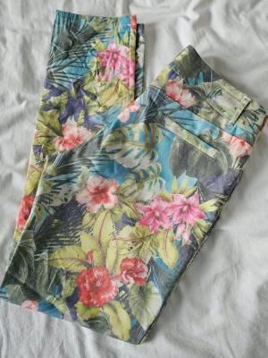 Färgglada sommarjeans(lågmidjade)med blommönsterS/M– Oanvända - Säljer ett par helt oanvända och unika lågmidjadejeans med ett fantastiskt tropiskt blommönster. De köptes i en lokal butik på Sicilien för flera år sedan, men har tyvärr bara blivit liggande i garderoben.Material: 95% Bomull, 5% Elastan. Small / 36 (motsvarar ca W28-W29 / L 29 i jeansstorlek)märkt med M men italiensk. Midjehöjd (gren till linning): 20 cm (låg midja) Innerbenslängd: 73 cm Benöppning (fåll nertill): 15 × 2 cm  👗👙👒🩴🧚‍♀️💃se fler av mina plagg ❤️