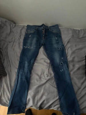 Blå slitna jeans från Dsquared2 - Säljer ett par blå jeans från Dsquared2 med snygga slitningar och distressed detaljer. Jeansen har klassisk femficksmodell och raka ben. Perfekta för dig som gillar en trendig och avslappnad stil.