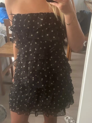 Svart prickig volangklänning - Axellös, storlek S. Inga shorts under kjolen, har dragkedja vid sidan. Aldrig använd, prislapp kvar!
