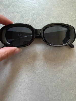 Svarta solglasögon från BikBok - Snygga svarta solglasögon från BikBok med rektangulära bågar och mörka glas. Klassisk och stilren design som passar till alla outfits. Perfekta för soliga dagar och ger en cool vibe.