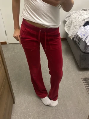 Juicy Couture - Snygga röda mjukisbyxor i velour med raka ben och snörning i midjan. Byxorna har två fickor fram och är perfekta för en avslappnad och chill look. Passar dig som gillar att vara bekväm men ändå se cool ut.