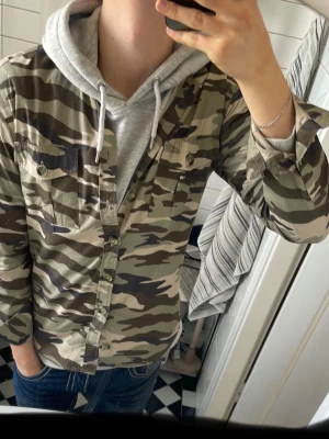 Camo overshirt med bröstfickor - Säljer en snygg overshirt i camouflage-mönster med beige, gröna och bruna toner från la chemise . Skjortan har två bröstfickor med knappstängning och klassisk krage. Tillverkad i ett lätt bomullstyg som är perfekt att ha över en hoodie eller t-shirt. Ge gärna pris förslag. 