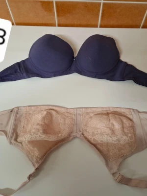 Lila och beige bh med spetsdetaljer - Två bhar till salu, en lila med släta kupor och en beige med vackra spetsdetaljer. Båda har bygel och justerbara axelband. Perfekt för dig som vill ha både stil och komfort.