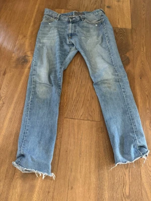 Ljusblå Acne Jeans med råa kanter - Säljer ett par ljusblå jeans från Acne Jeans med raka ben och slitna, råa kanter nertill. Klassisk femficksmodell i denim med snygg tvätt och subtila slitningar på benen. Perfekta för en avslappnad och trendig look.