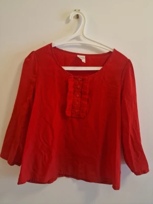 Röd blus med knappar från Monki - Snygg röd blus från Monki med rund halsringning och dekorativa knappar framtill. Blusen har långa ärmar och ett coolt rynkat parti vid knappraden. Perfekt för dig som vill ha en färgstark och trendig look.