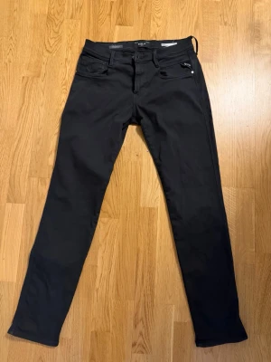 Replay anbass hyperflex 30/32  - Säljer ett par svarta jeans från Replay med klassisk femficksdesign och raka ben. Jeansen har diskreta detaljer och är tillverkade i ett stretchigt material som ger en skön passform. Perfekta för dig som gillar en stilren look.