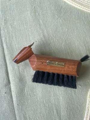 Träborste formad som häst - Unik vintage borste i trä formad som en häst, med svart borst och detaljer som öron och svans. Tillverkad i Sverige och har en snygg retrostil. Perfekt som dekoration eller för att borsta av kläder och skor.