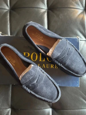 Mörkblå mockaloafers Polo Ralph Lauren - Snygga mörkblå loafers i mocka från Polo Ralph Lauren. Klassisk penny loafer-design med sömmar runt tån och diskret logga på innersulan. Skorna har en stilren och tidlös look som passar till många outfits. Nypris 2500
