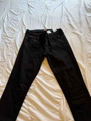 Svarta jeans Tommy Jeans Nora Mid - Snygga svarta jeans från Tommy Jeans, modell Nora Mid. Jeansen har klassisk femficksdesign, raka ben och normal midja. Materialet är stretchigt för extra komfort och passform. Perfekta för en trendig och avslappnad look.