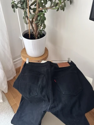 Svarta Levi's jeans med rak passform - Säljer ett par svarta jeans från Levi's med klassisk rak passform och femficksdesign. Jeansen har tydlig läderpatch bak i midjan och den ikoniska röda Levi's-taggen på bakfickan. Perfekta för en stilren och avslappnad look.