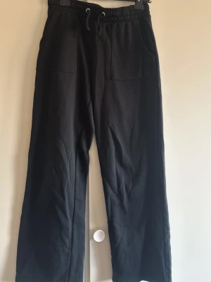 Svarta mjukisbyxor med raka ben - Svarta mjukisbyxor med raka ben och resår i midjan samt dragsko. Byxorna har två stora fickor fram och är tillverkade i mjukt och bekvämt tyg. Perfekta för en avslappnad stil.