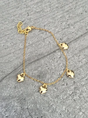 Guldfärgat armband med hjärtberlocker - Snyggt handgjort armband i guldfärg med fyra små hjärtformade berlocker som hänger längs en tunn kedja. Armbandet har justerbar längd med förlängningskedja och är perfekt för dig som gillar stilrena och söta accessoarer. Kedjan är guldtonat rostfritt stål.