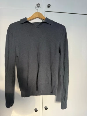 Grå merinoulltröja med krage - Snygg grå långärmad tröja från These Glory Days i mjuk merinoull. Tröjan har klassisk krage och V-ringning, perfekt för en stilren look. Enkel att matcha med jeans eller chinos.