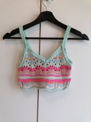 Pastellfärgad stickad crop top - En handstickad crop top i pastellfärger från Pull & Bear. Toppen har ett vackert hålmönster och färger i mintgrönt och rosa. Perfekt för stranden, sommaren och festivaler. Materialet känns mjukt och luftigt. 