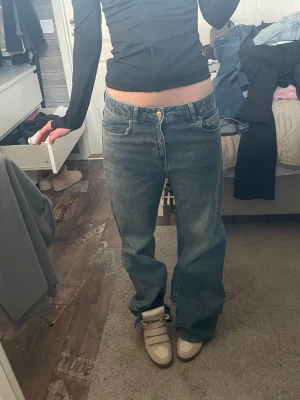 Baggy blå jeans med raka ben - Säljer ett par baggy blå jeans med raka ben och klassisk femficksdesign. Jeansen har låg midja och är tillverkade i denim. Perfekta för en avslappnad och trendig stil.