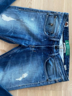 Blå slitna jeans från Kuyichi - Säljer ett par blå jeans från Kuyichi med slitningar och tvättade detaljer. Klassisk femficksmodell med knappgylf. Snygga detaljer som knapp på myntfickan och kontrastsömmar. Perfekta för en avslappnad streetstil. Priser går alltid att diskutera och fråga gärna om ni undrar något! 