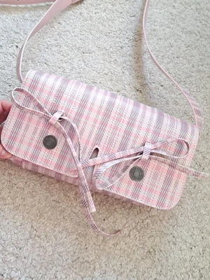 Rutig rosa handväska med rosetter - supersöt rosa handväska med rutigt mönster och rosetter med justerbart axelband. säljer pga att den aldrig kommer till användning💕