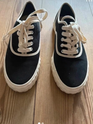Svarta canvas sneakers med beige  sula - Svarta sneakers i canvas med beige tjock sula och vita snören. Skorna har en klassisk låg modell med vita detaljer runt snörningen och längs kanten. Perfekta för en avslappnad och stilren look. Storlek 38 .Helt oananvända hm märke 