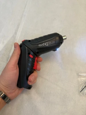 Svart och röd sladdlös skruvdragare - Praktisk sladdlös skruvdragare i svart plast med röda detaljer. Ergonomiskt handtag och LED-lampa framtill för bättre sikt. Perfekt för mindre byggprojekt och montering. Kommer med några bits som syns på bilden.