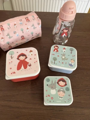 Rosa matlådeset med Rödluvanmotiv - Säljer ett set med tre matlådor, en vattenflaska och en necessär från Tutete. Alla delar har gulliga Rödluvan-motiv i rosa, rött och grönt. Matlådorna är fyrkantiga och flaskan har ett praktiskt sugrör. Perfekt för lunch eller utflykt.