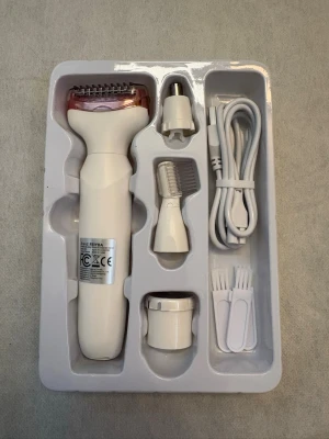 Lady Shaver Beauty Kit - Multifunktionell elektrisk rakapparat med fyra utbytbara huvuden: skäggtrimmer, kroppsrakare, nästrimmer och ögonbrynstrimmer. Vit och rosa design, laddas via USB och inkluderar rengöringsborstar och kabel. Perfekt för smidig och hygienisk grooming.