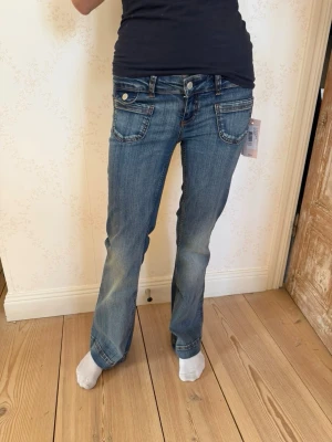 Blå lågmidjade bootcut jeans - Snygga blå bootcut jeans med stora framfickor och markerade sömmar. Jeansen har låg midja och klassisk femficksdesign med detaljerade nitar. Nypris 600 kr!!💙 Storlek 36/short