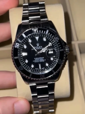 Rollie date - Säljer en klassisk Submariner med svart urtavla och silverfärgad länk i metall. Klockan har tydliga vita markeringar, datumfönster med förstoringsglas och vridbar svart bezel. Perfekt för dig som gillar stilrena och exklusiva accessoarer. Finns 2 klockor tillgängliga, svart och grön…Kolla på andra annonsen som har FRI FRAKT