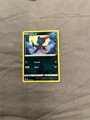 Pokémonkort Sneasel - Pokémonkort med motiv av Sneasel. Kortet har en svart bakgrund med gula kanter och visar Sneasel i en actionpose. Tillverkat i laminerad papp med tryckt bild och text. Perfekt för samlare eller Pokémon-entusiaster.
