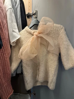 Krämvit fluffig kofta med rosett - Köpte den förra julen aldrig använt bara provat💕Supersöt krämvit kofta i fluffigt material med en stor, transparent rosett i beige vid halsen. Koftan har trekvartsärmar och en mjuk, mysig känsla. Perfekt för dig som vill ha något gulligt 