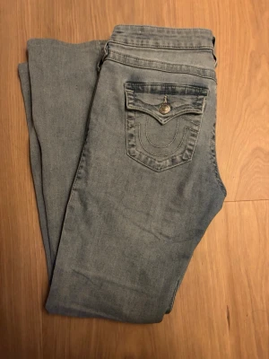 Ljusblå True Religion jeans Joey - Säljer ett par ljusblå jeans från True Religion, modell Joey med låg midja. Jeansen har klassiska sömmar och en ficka med lock och knapp bak. De är något uppsydda, typ 5 cm och passar mig som är 167. De har någon färgning längst ner men gör säkert bort i tvätten, kommer att tvättas innan de skickas.