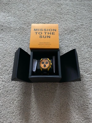 Omega x Swatch MoonSwatch Mission To The Sun Remake - Säljer en Omega x Swatch MoonSwatch Mission to the Sun. Klockan har en gul boett i biokeramik, svart bezel och orange urtavla med svarta detaljer. Snygg och unik design med Omega-logga på bandet. Kommer i originalförpackning.