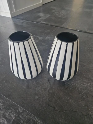 Två svartvita randiga vaser - Säljer två konformade vaser i keramik med svartvita vertikala ränder. De har en modern och stilren look som gör dem till perfekta detaljer för ditt rum. Passar både till blommor eller som dekoration på hyllan.