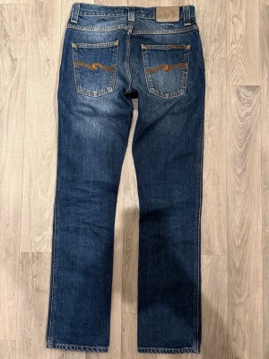 Nudie Jeans Slim Jim Orange Embo Blå W29/L32 Slim Fit - Nudie Jeans Slim Jim Orange Embo blå jeans i clean tvätt, slim fit modell som sitter bra och funkar till allt, storlek W29/L32, midja 37,5 cm, ytterbenslängd 100,5 cm, benöppning 18 cm, i fint skick.
