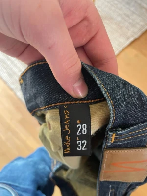 Mörkblå jeans från Nudie Jeans - Snygga mörkblå jeans från Nudie Jeans med klassiska kontrastsömmar och ikoniska broderade bakfickor. Jeansen har rak passform och är tillverkade i slitstarkt denimtyg. Perfekta för en cool och avslappnad stil.