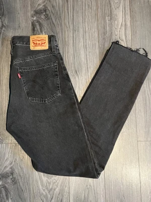  Levi's 501 - Få tag på dessa ikoniska Levi’s 501- jeans kända för sin klassiska raka passform, medelhög midja och en knappgylf. Tillverkade i kraftig denim med snygg ”faded black” tvätt och råa benslut Den vintageinspirerade råa stilen ger en tidlös känsla till din garderob, och den blekta svarta färgen är lätt att matcha med alla outfits. Mått :  Midja: 79 cm ( 39 cm platt mätt )  Innerbenslängd: 79 cm Grenhöjd : fram 28 cm / back 40 cm  Benöppning: 18 cm  