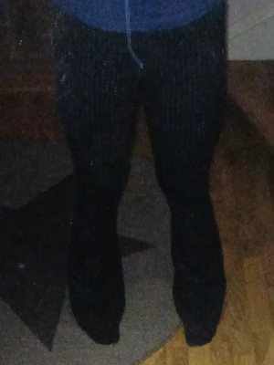 Svarta kostymbyxor med kritstrecksränder - Snygga svarta kostymbyxor med vita kritstrecksränder och utsvängda ben. Byxorna har hög midja och klassisk passform, perfekta för en stilren look. Materialet ser ut att vara en mjuk och följsam textil som ger en dressad känsla.