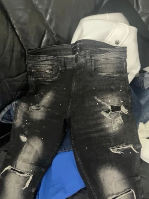 Supply & Demand jeans - Svarta jeans från Supply & Demand med slitna detaljer, dragkedja vid fickan och coola slitningar på benen. Jeansen har en tight passform och är dekorerade med små vita färgstänk för en edgy look.